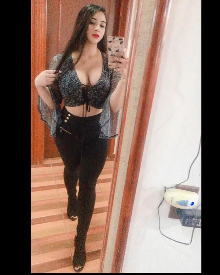 Jeune femme aux cheveux bruns portant un haut noir et un short noir, prenant un selfie dans un miroir