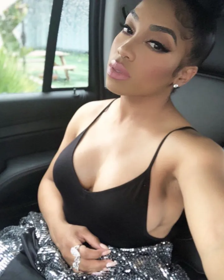 Femme aux cheveux noirs, regardant vers le côté, portant un haut noir et une jupe scintillante, assise dans une voiture.
