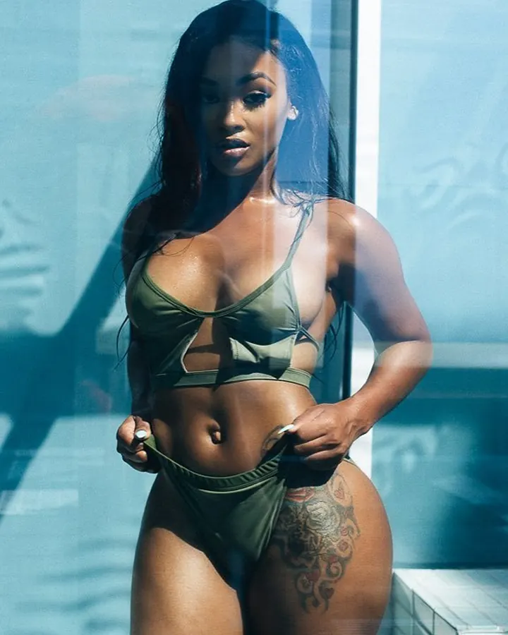 Femme aux cheveux noirs portant un bikini vert, posant près d'une piscine avec un tatouage sur la cuisse