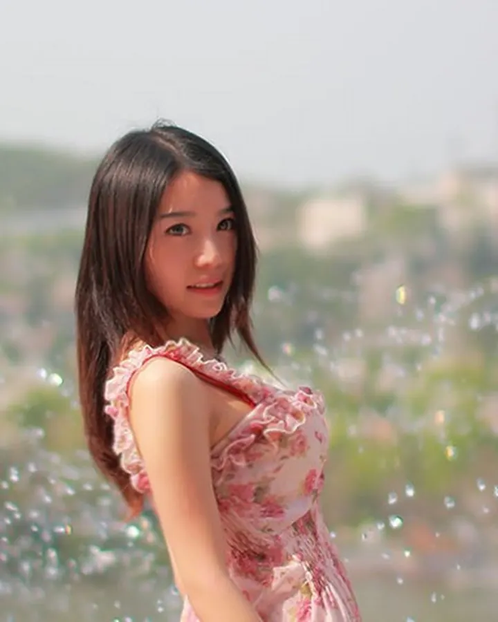 Jeune femme asiatique aux cheveux châtains portant une robe fleurie rose, souriant devant un arrière-plan flou avec des bulles.