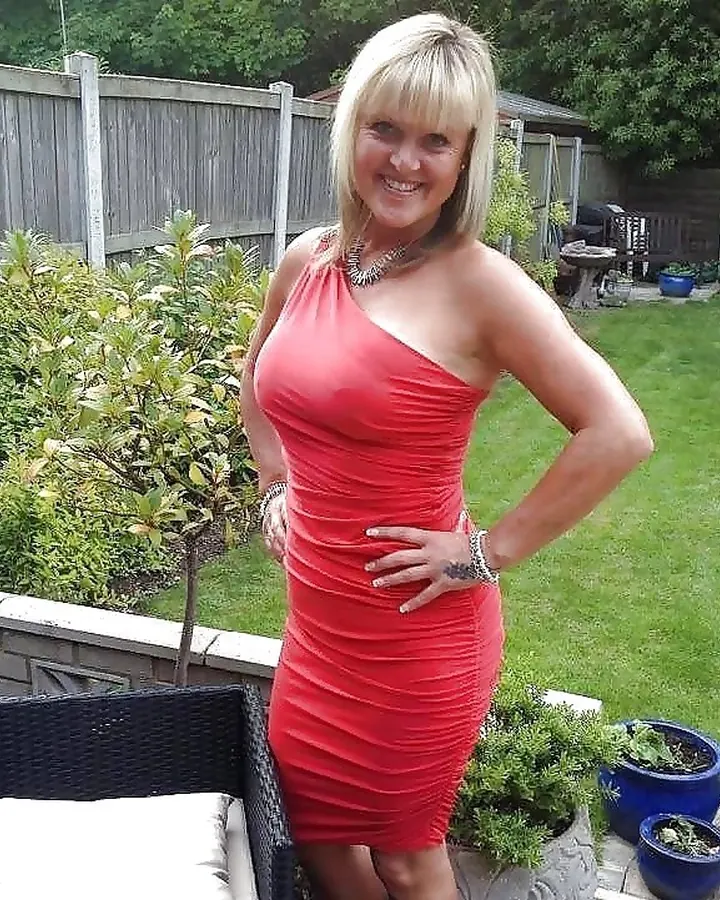 Femme blonde, portant une robe rouge, posant dans un jardin.