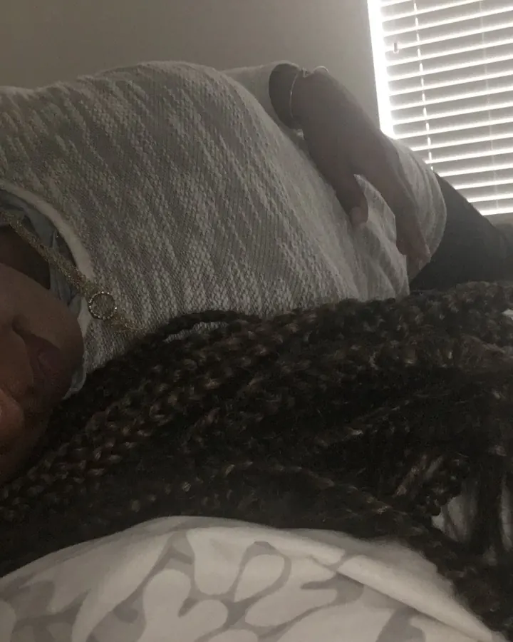 Femme allongée sur un lit, regardant vers la caméra, cheveux tressés, couverture grise