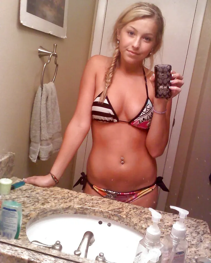 Jeune femme blonde en bikini, prenant un selfie devant un miroir de salle de bain