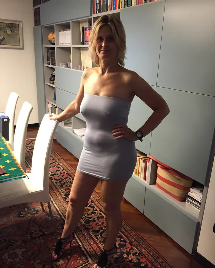 Femme en maillot gris, assise sur un tapis moelleux, prenant un selfie, pieds en sandales fourrées.
