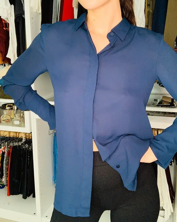 Jeune femme aux cheveux bruns, en haut bleu, mains sur les hanches, devant un dressing