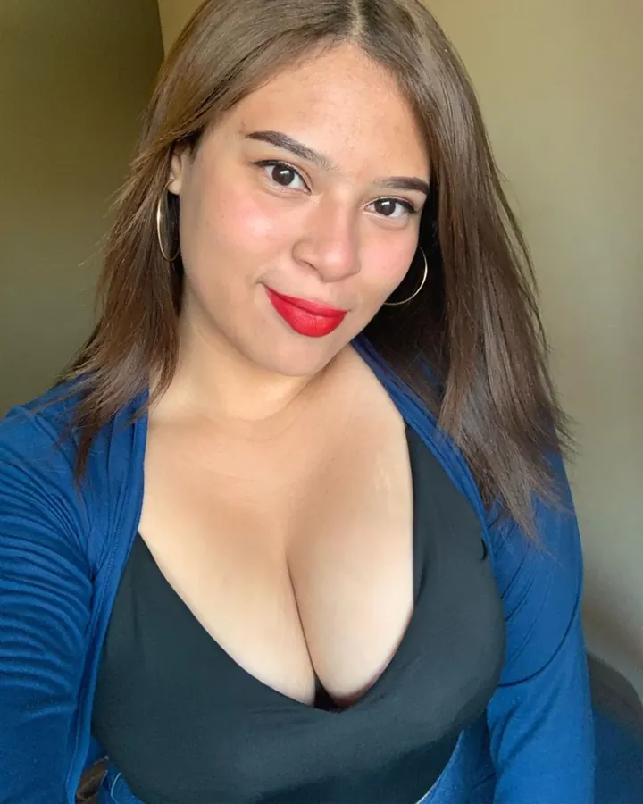 Femme aux cheveux châtains en haut noir et cardigan bleu, souriante, regardant l'appareil photo, rouge à lèvres rouge.