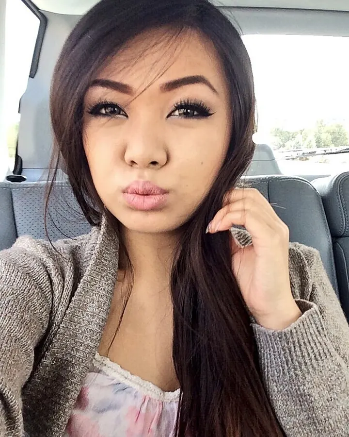 Jeune femme asiatique aux cheveux noirs, en sous-vêtements noirs, prenant un selfie dans une voiture.