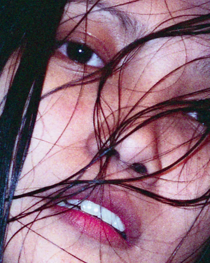 Plan rapproché du visage d'une femme aux cheveux noirs, avec des mèches devant les yeux, souriant légèrement