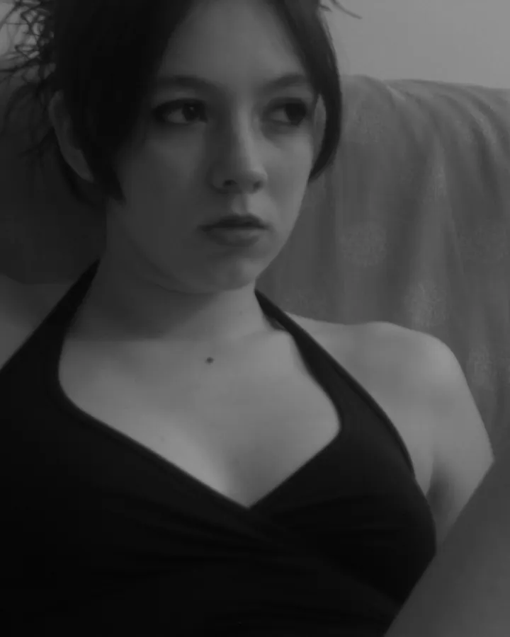 Femme en noir et blanc, assise sur un canapé, portant un haut noir, regardant vers le côté