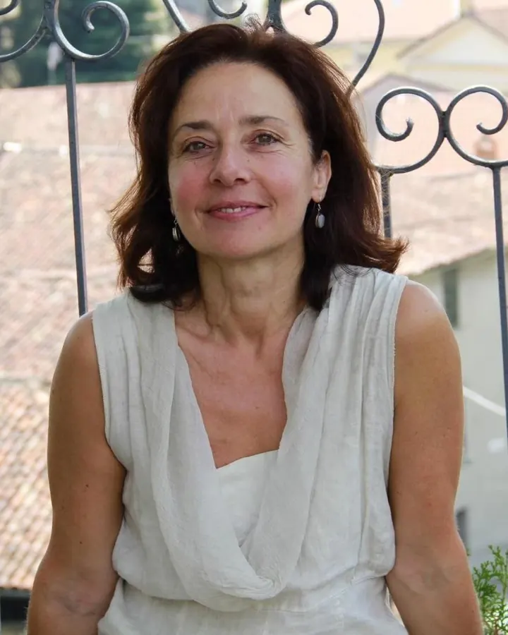 Femme aux cheveux châtains en robe blanche, souriant devant une grille métallique