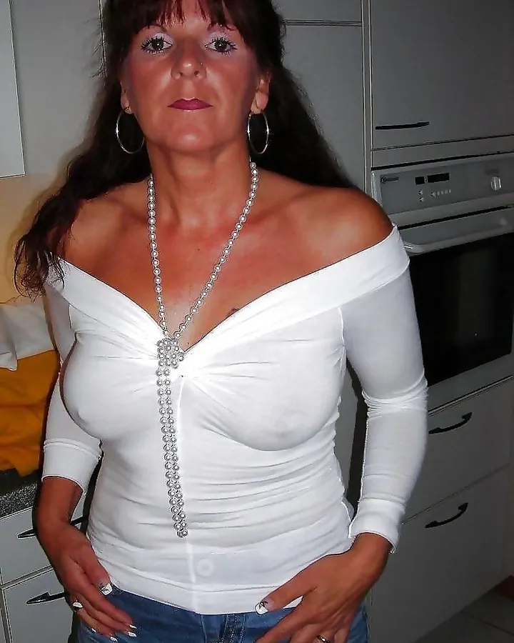 Femme aux cheveux longs bruns, en robe noire, pose sur un lit, mains sur les hanches
