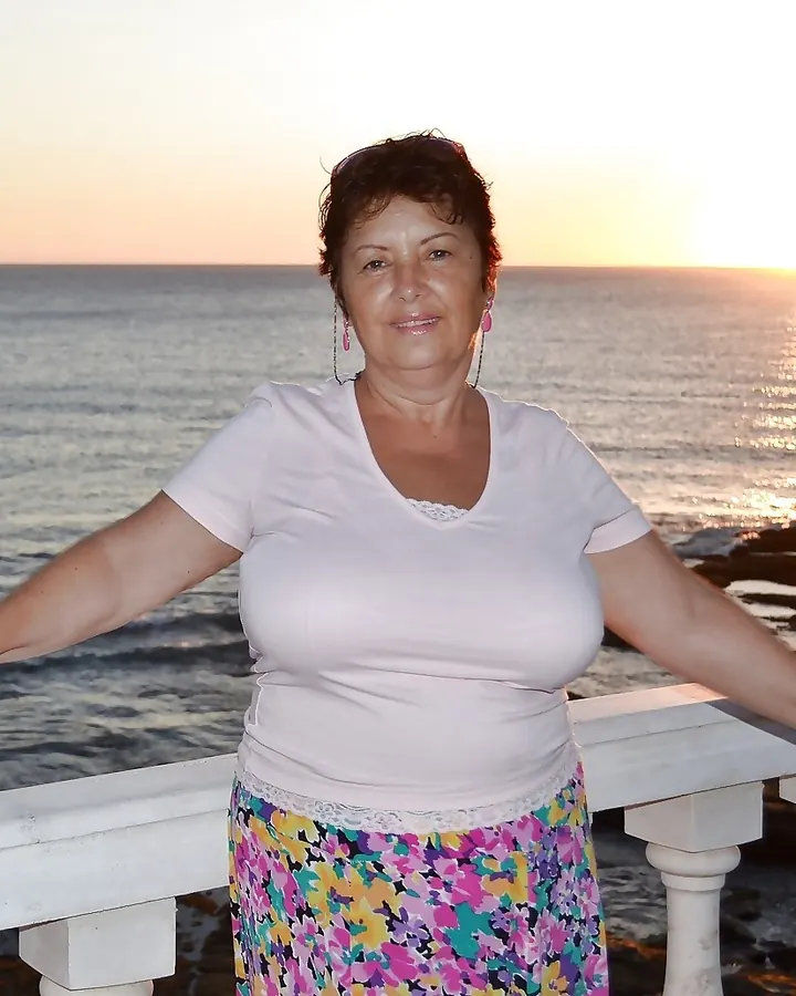 Femme rousse en robe rose, posant dans un salon avec un canapé beige.