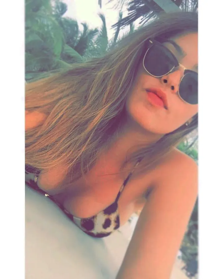 Femme aux cheveux blonds, portant un maillot de bain léopard, des lunettes de soleil, prenant un selfie en extérieur.