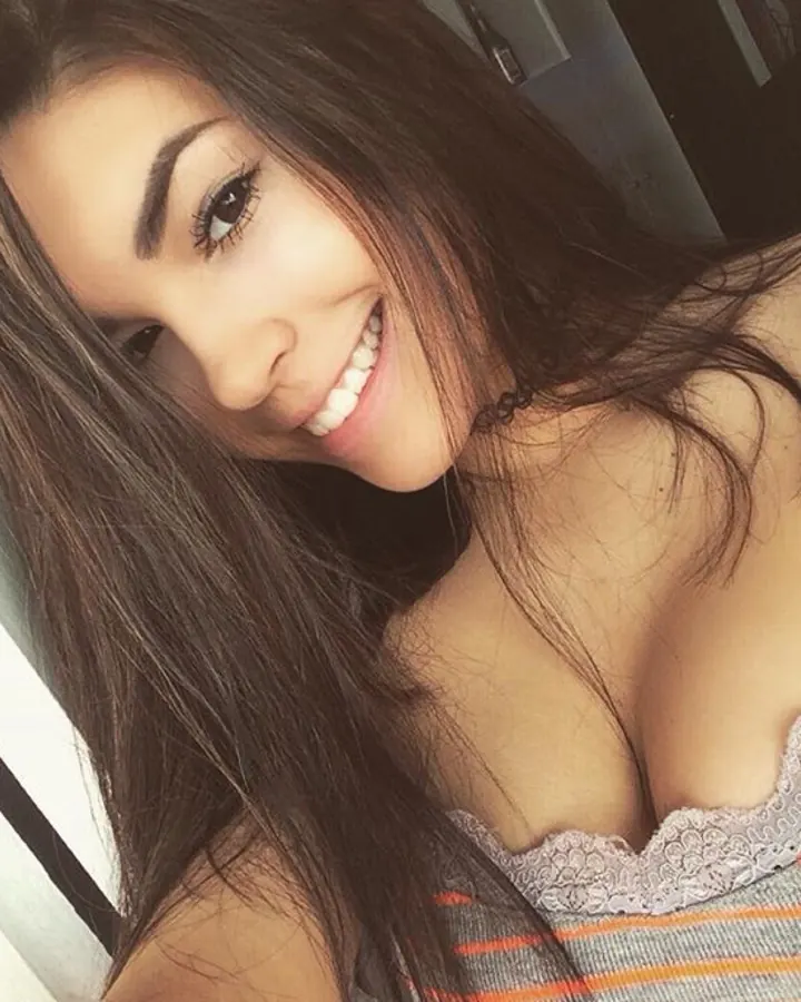 Femme souriante, aux cheveux bruns foncés, portant un haut à dentelle gris et un débardeur rayé, en gros plan