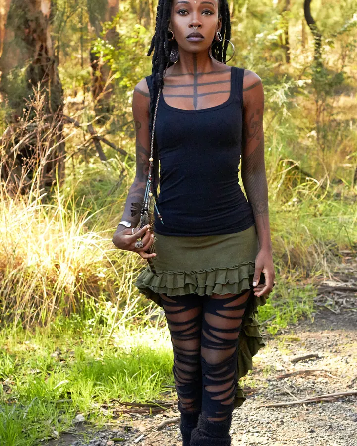 Femme africaine en haut noir et jupe verte, debout dans une forêt