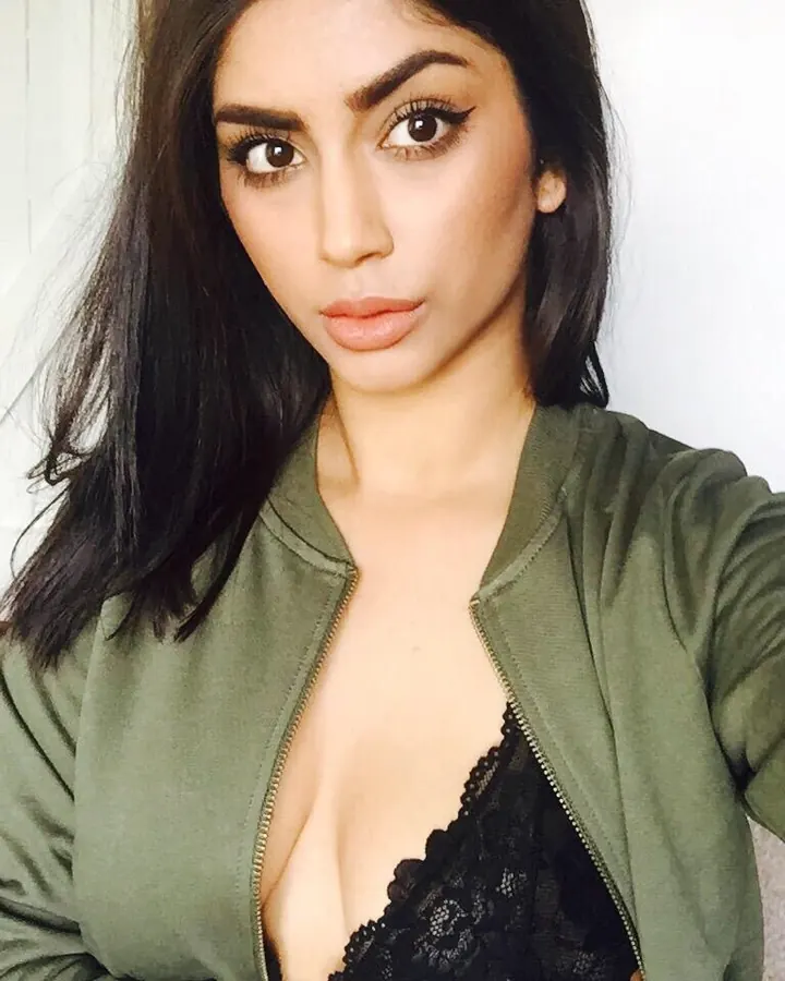 Femme aux cheveux bruns, vêtue d’un haut noir, prenant un selfie dans un environnement intérieur moderne, regardant l'appareil.