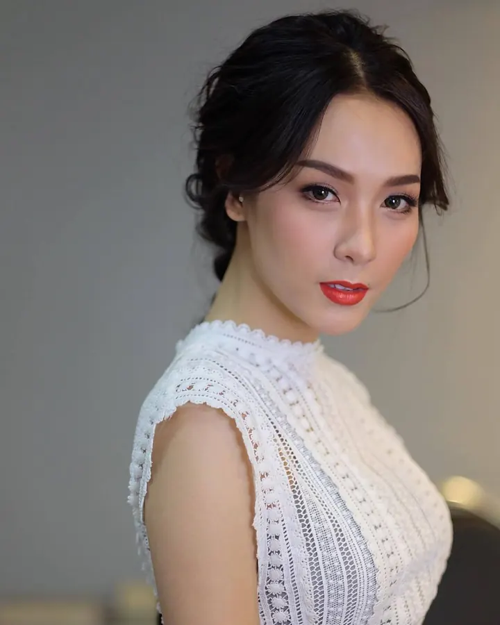 Femme asiatique aux cheveux bruns-noirs, portant un haut noir et un legging gris, prenant un selfie dans une salle de sport.